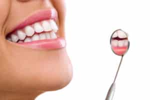 Woman smiling showing white teeth next to dental mirror on white background.