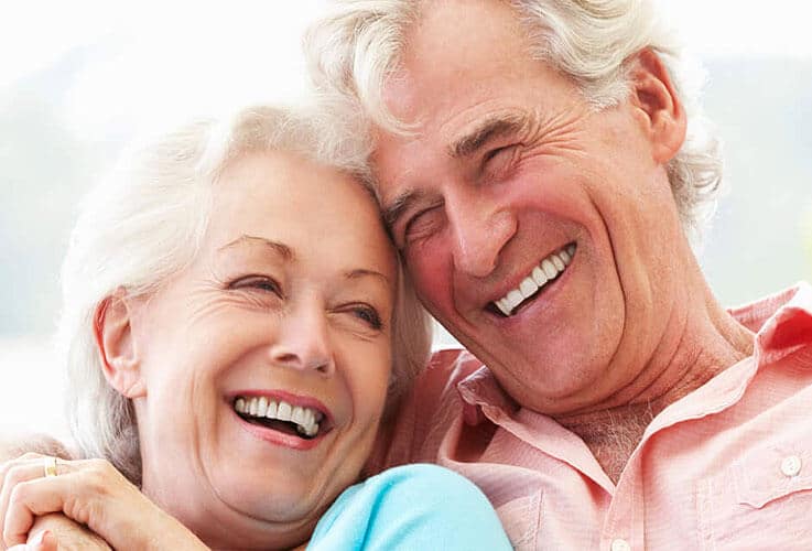 Happy senior couple embracing and smiling together outdoors in bright daylight.