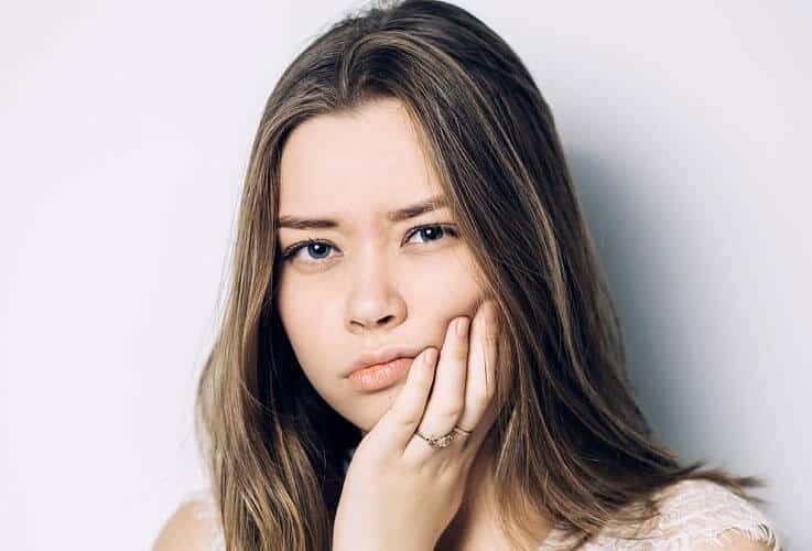 Young woman with long dark hair resting chin on hand against white background.