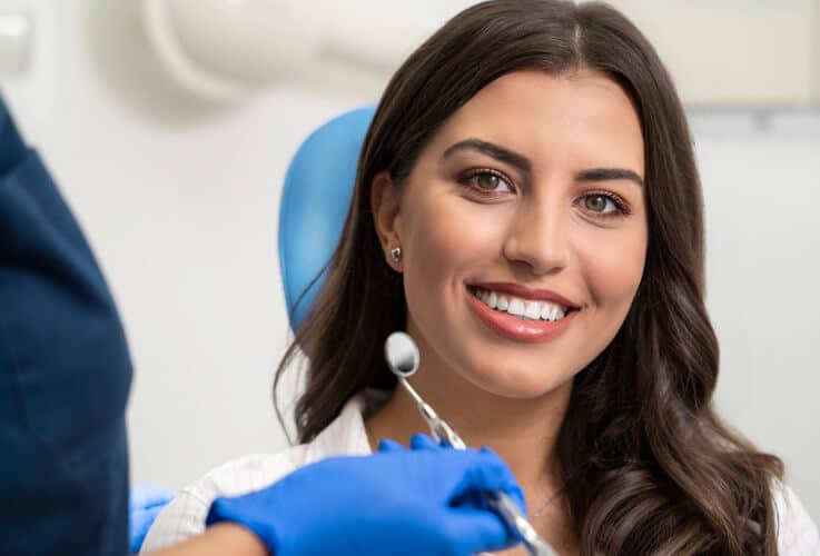 Woman smiling at dental office wearing blue gloves and bib