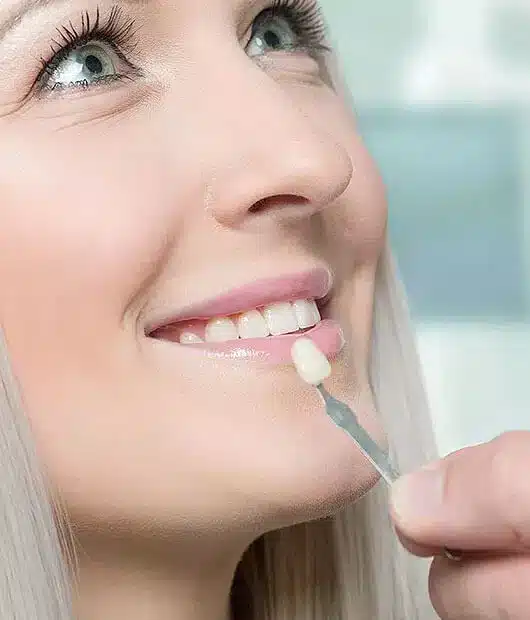 Woman applying lip gloss or lipstick with applicator brush in bright, modern setting.