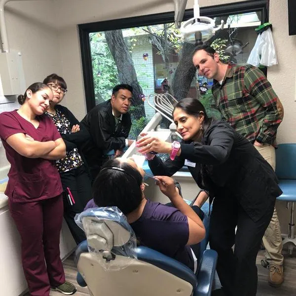 Dental professionals demonstrate procedure on patient in training setting with students observing.