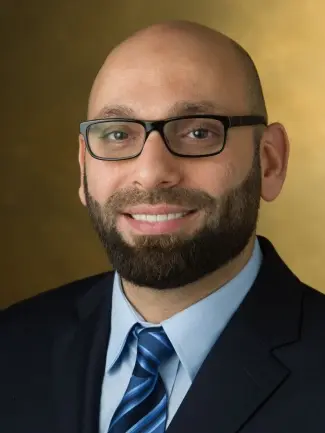Professional headshot of a male dentist wearing glasses and dark suit with blue striped tie.